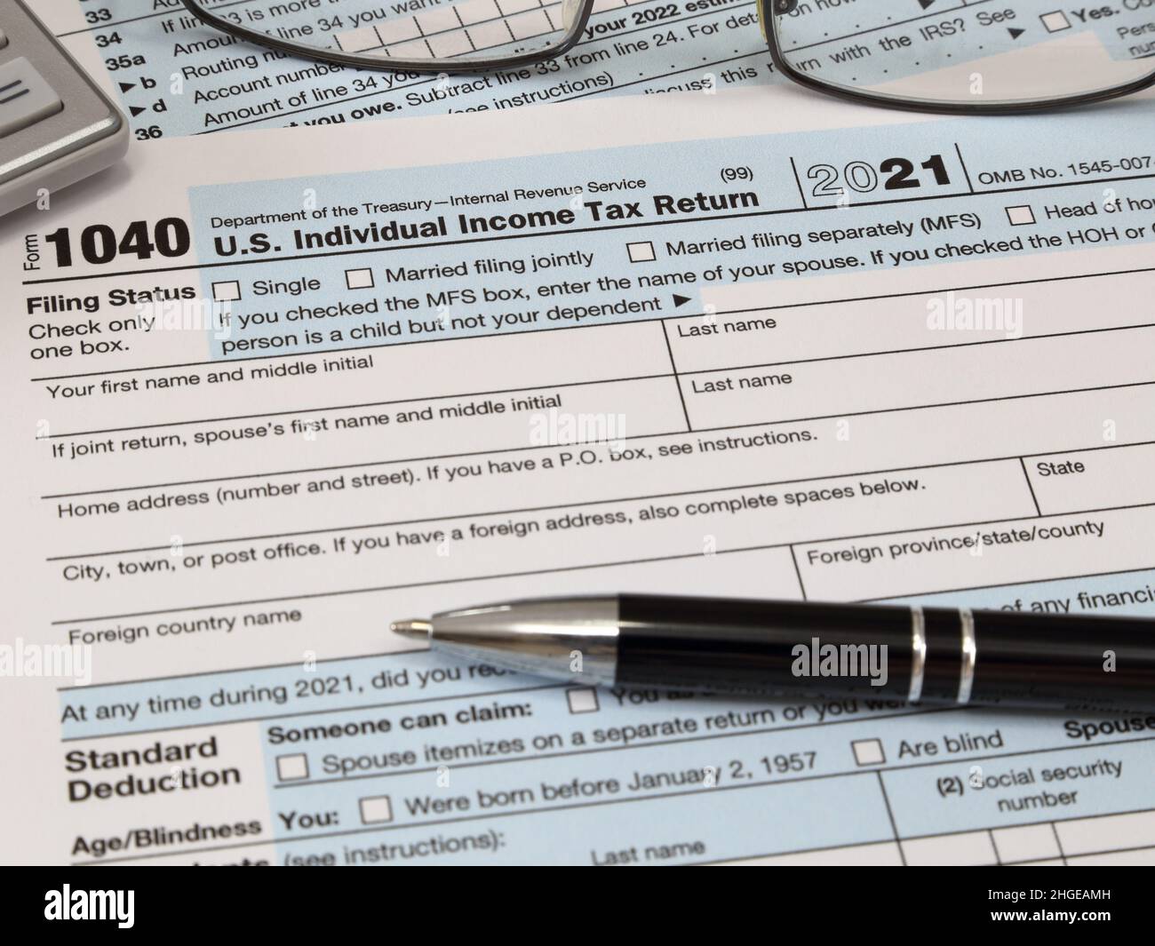 An IRS 1040 tax year 2021, along with an ink pen, calculator, and glasses. The Internal Revenue