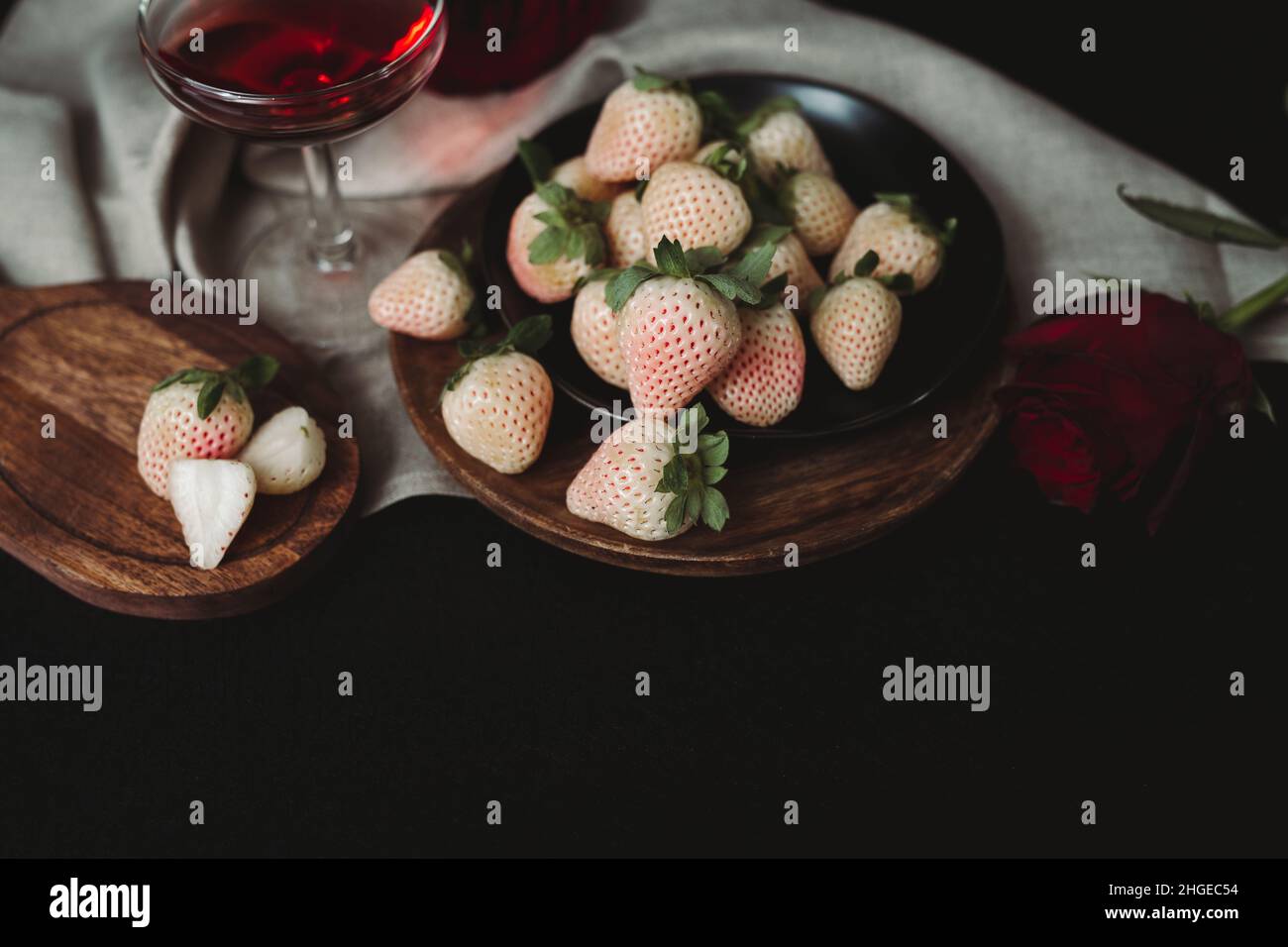 Moody Valentine Still Life. Pineberry on Wooden Plate with Dark Background. White Strawberry. Dark Valentine Aesthetic. Strawberries and Wine. Stock Photo
