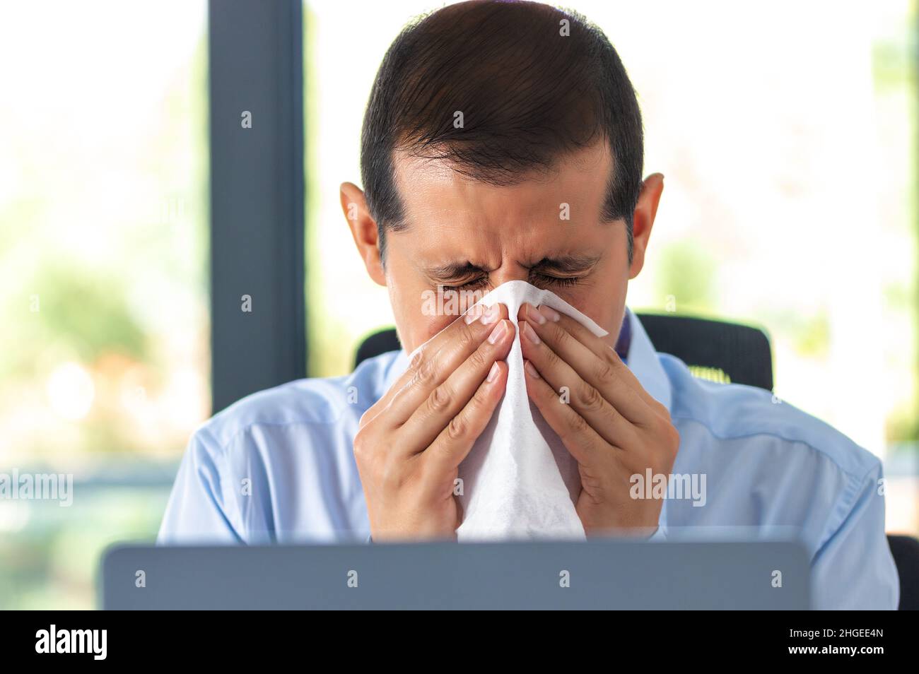Shot of a businessman blowing his nose with a tissue at work Stock Photo