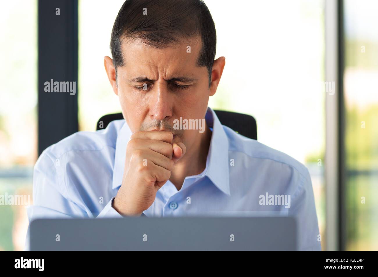 Cropped shot of a handsome young businessman sitting alone in his office and coughing as he suffers from a cold Stock Photo