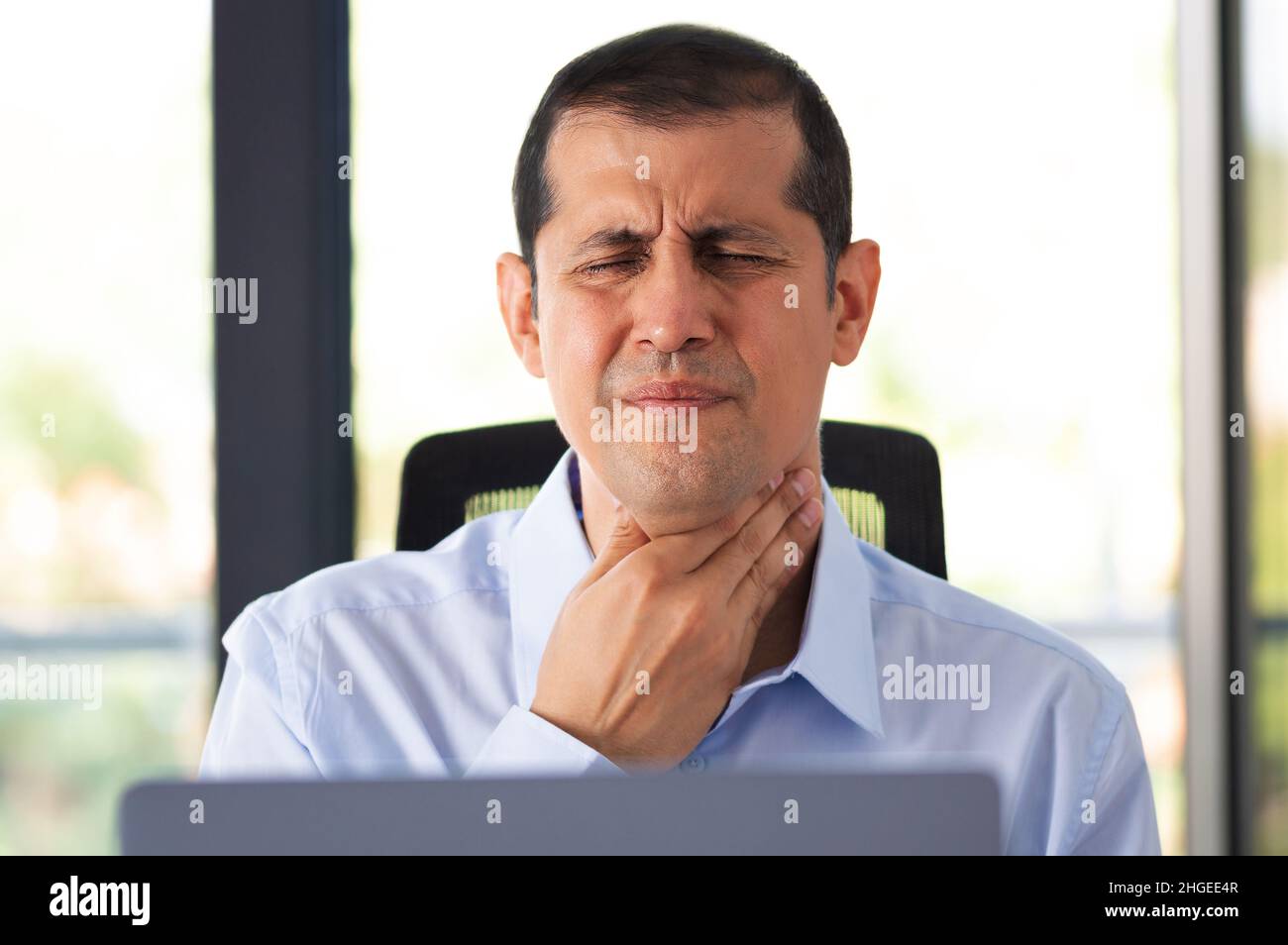 Shot of a young businessman experiencing throat pain while working in an office Stock Photo