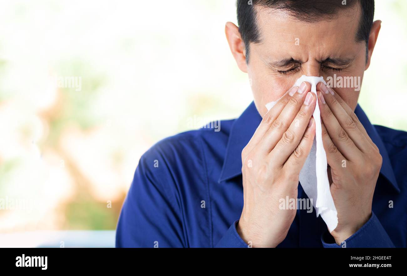 Shot of an young man feeling ill and blowing his nose with a tissue at home and copy space Stock Photo