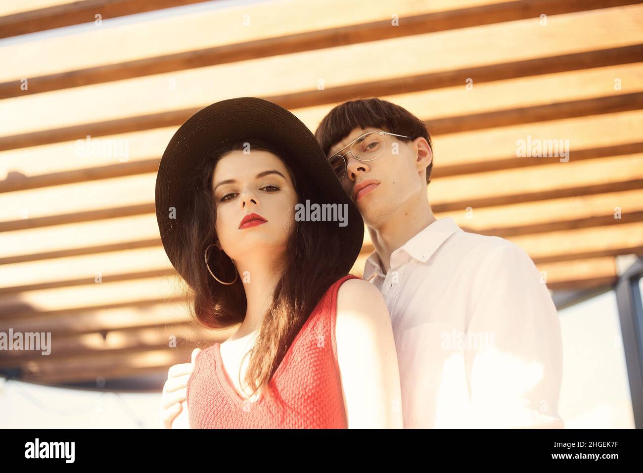 Beautiful fashionable couple on an abstract background. Fashionable hipsters. Girl in a red dress and black big hat. A man with glasses and a white sh Stock Photo