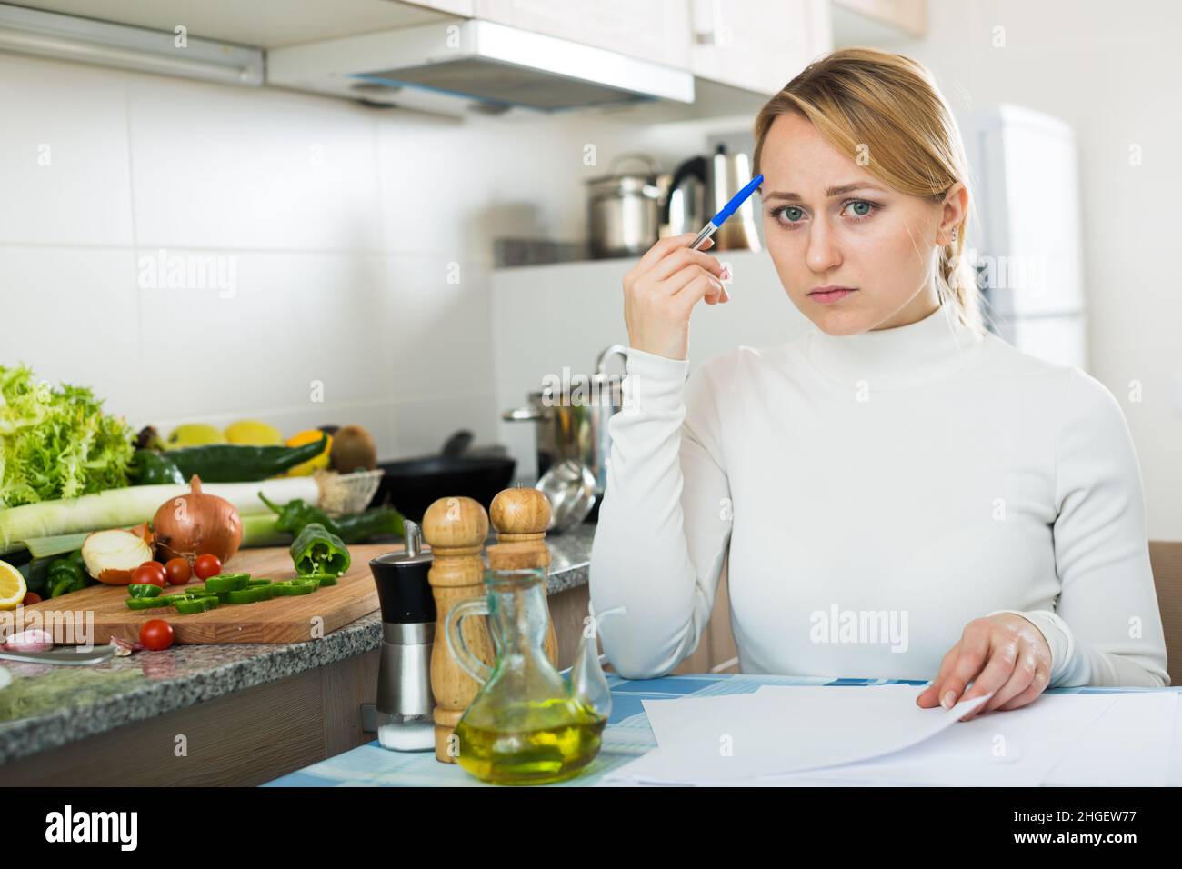 Sad housewife with documents in kitchen Stock Photo