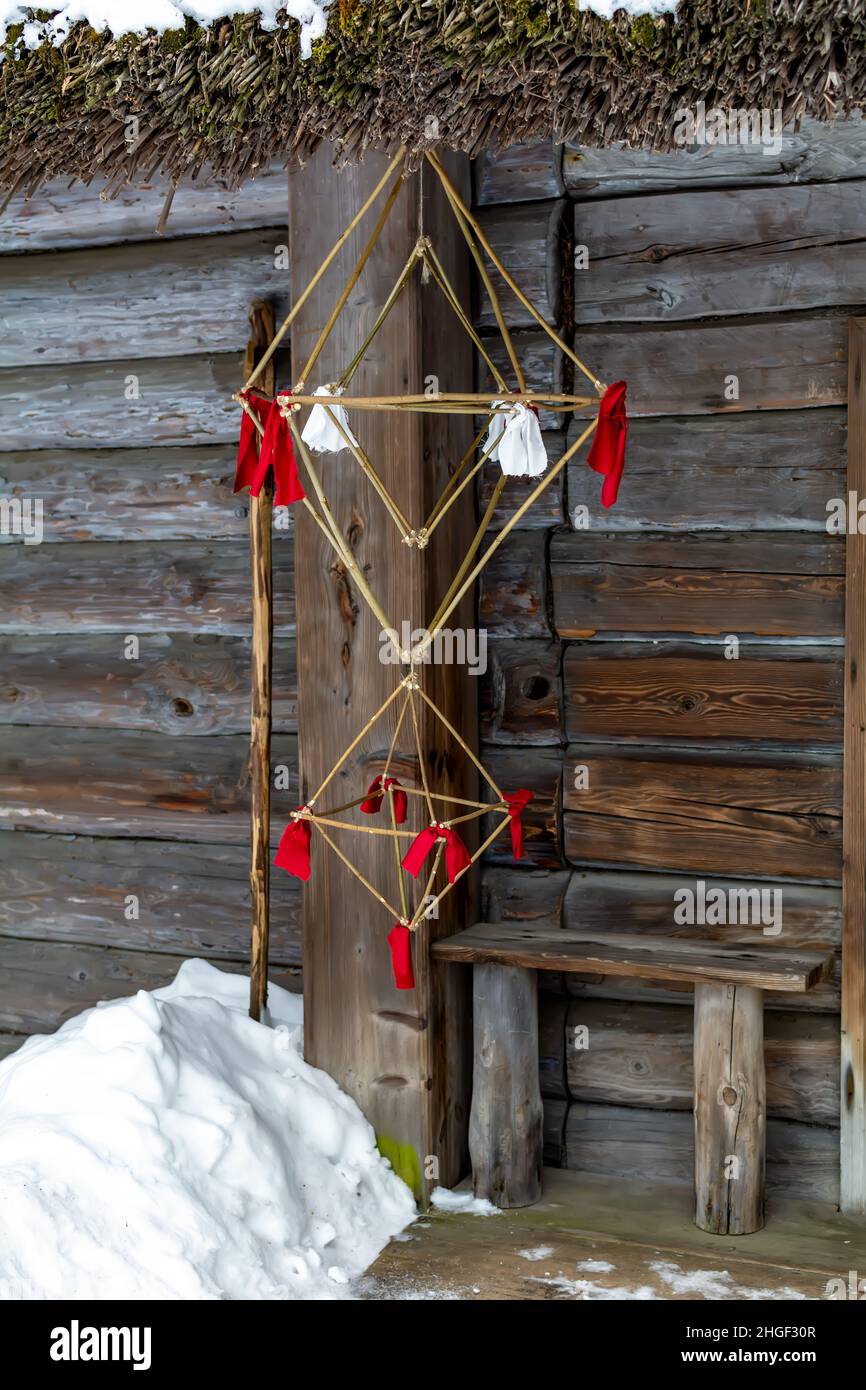 Latvian Puzurs with red ribbons hanging at log hut. Puzurs is traditional Latvian room decoration made of straws Stock Photo