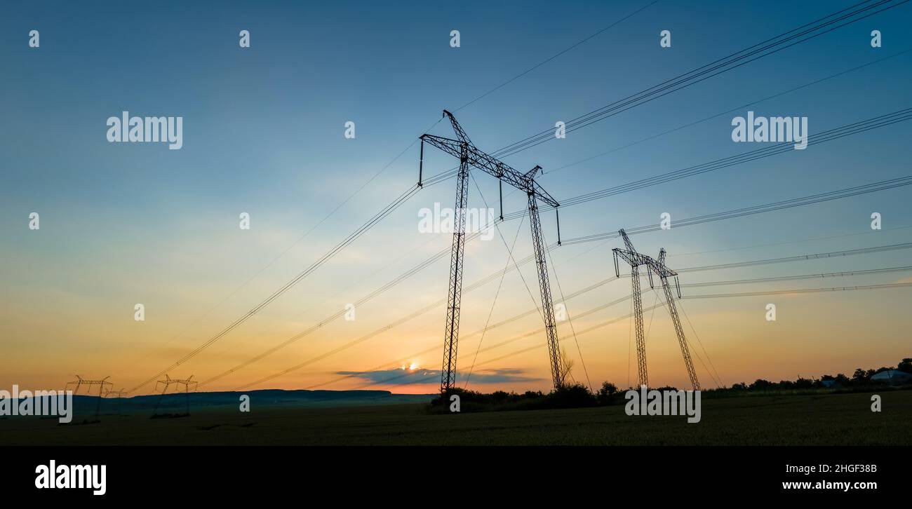 Dark silhouette of high voltage towers with electric power lines at ...