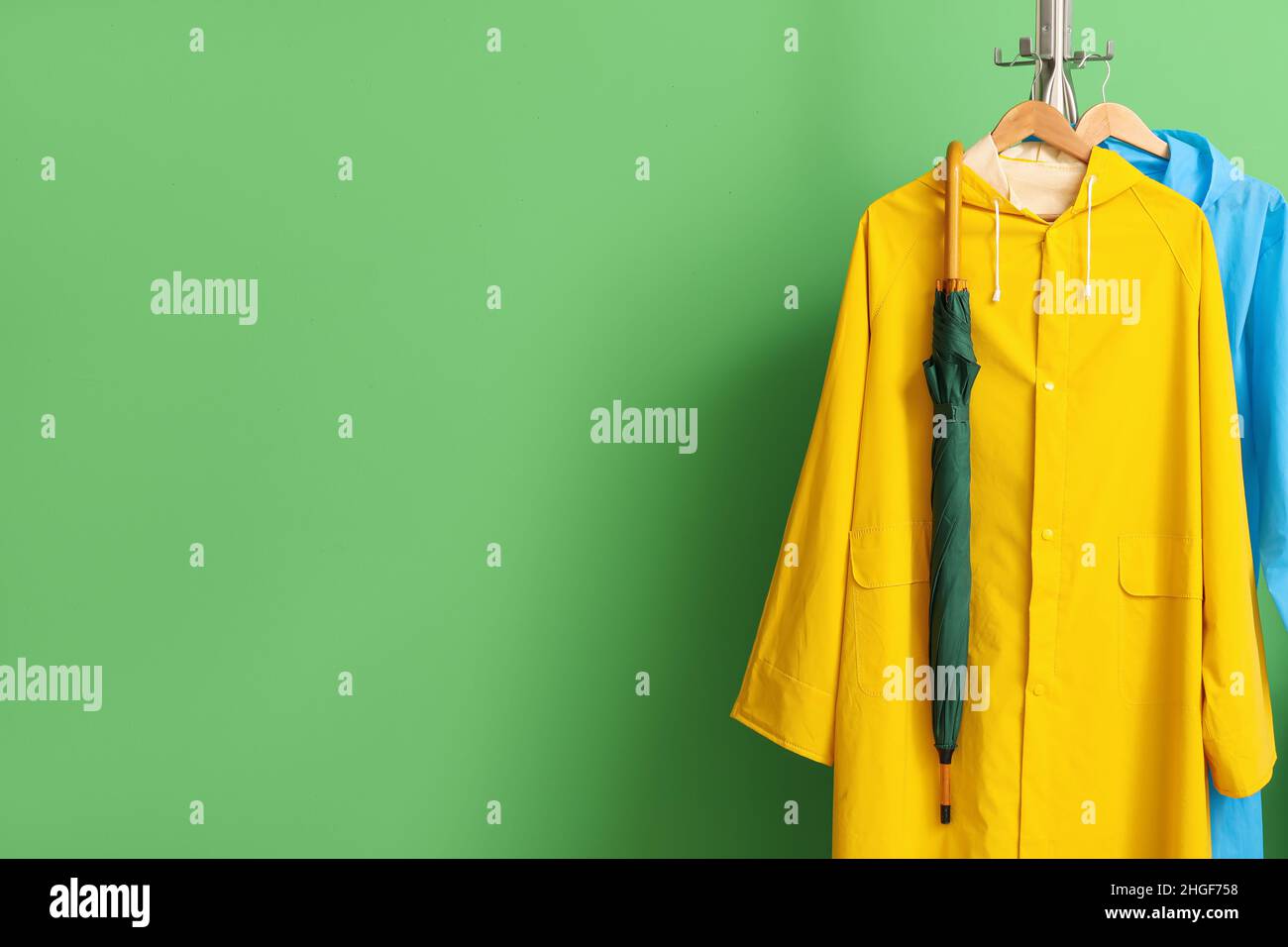 Rack with raincoats and umbrella near green wall Stock Photo Alamy