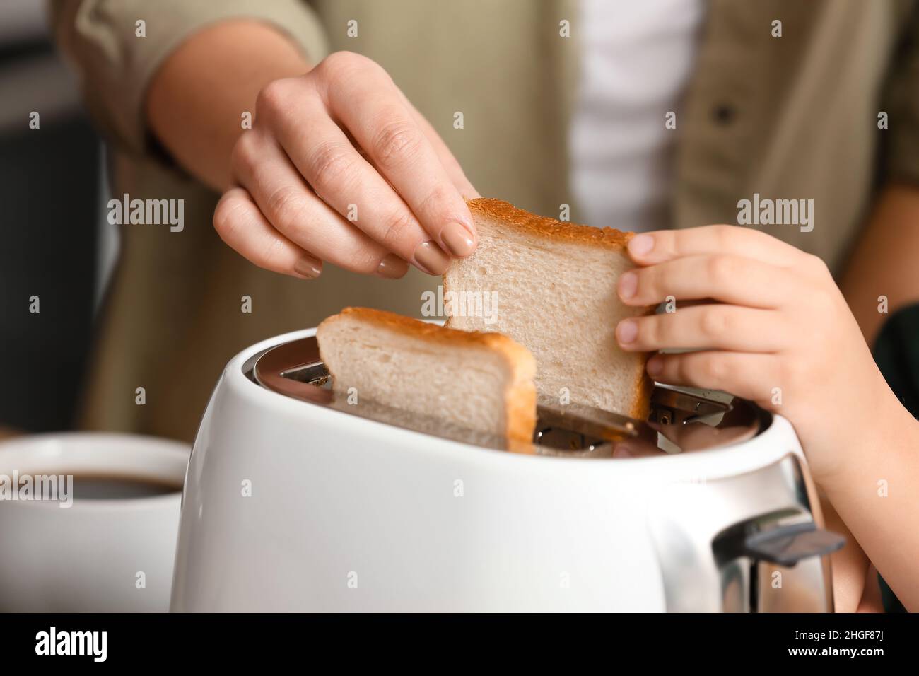 Little boy and his mother putting bread slices into toaster in kitchen ...
