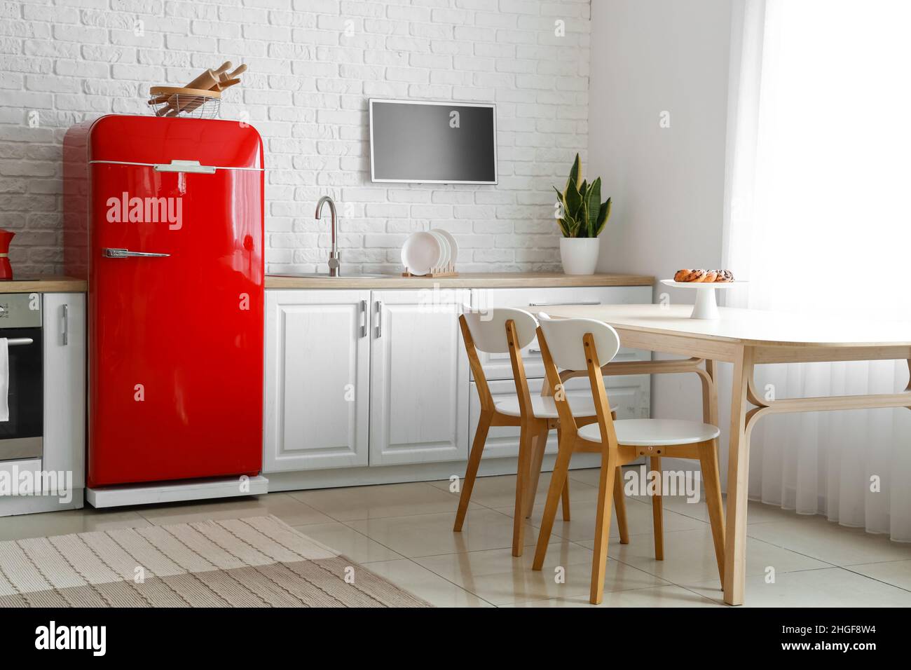 Interior of light kitchen with red fridge, white counters and dining ...