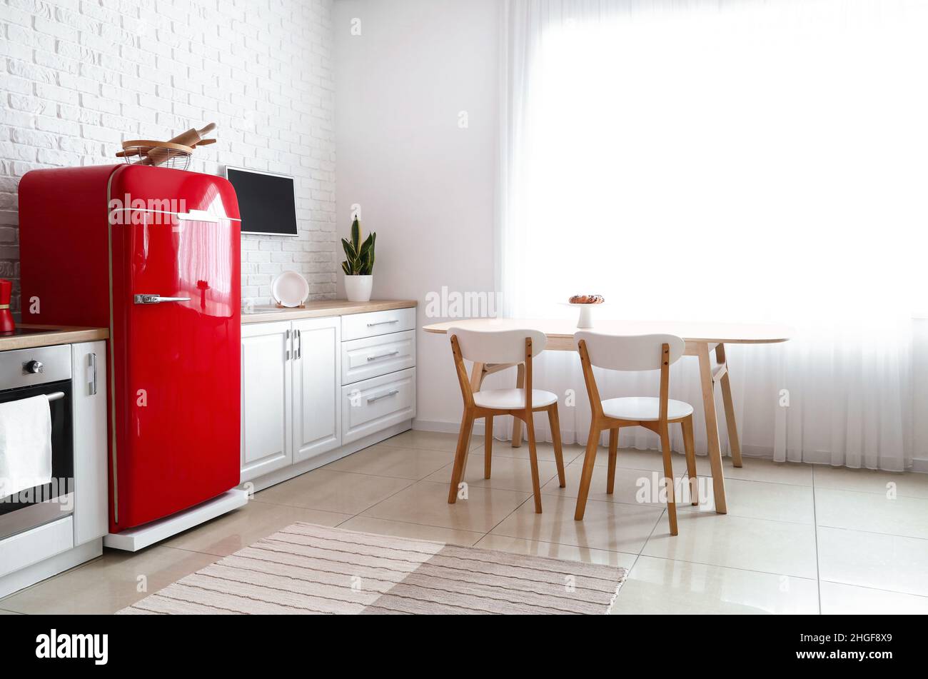 Interior of light kitchen with red fridge, white counters and dining ...