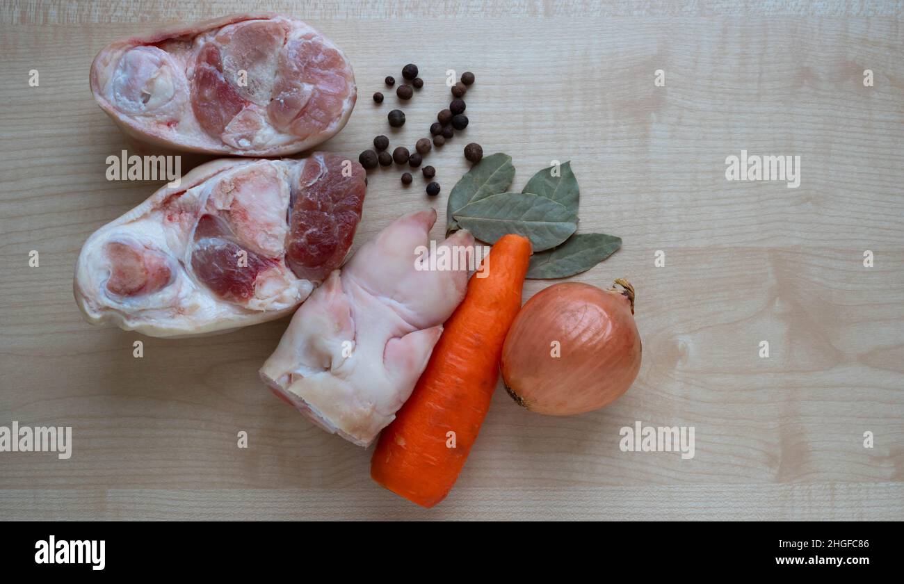 Raw pork meat and leg, carrots and onions on the kitchen table for making jelly. Stock Photo