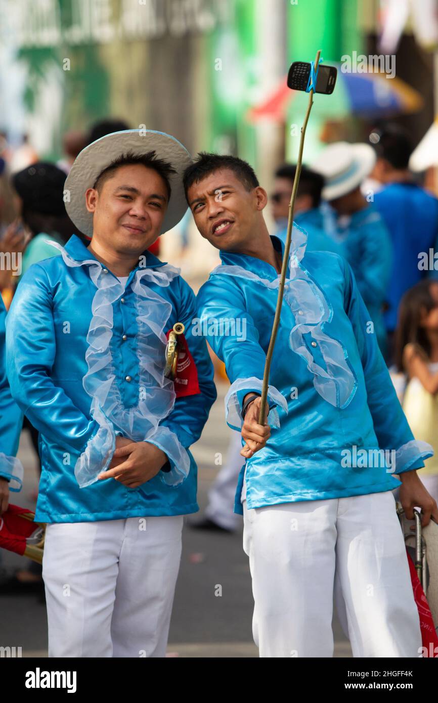 A man using a mobile phone tied to a bamboo stick during the Sinulog Festival in Cebu City, Philippines, using it to take an improvised photo with a friend. Stock Photo
