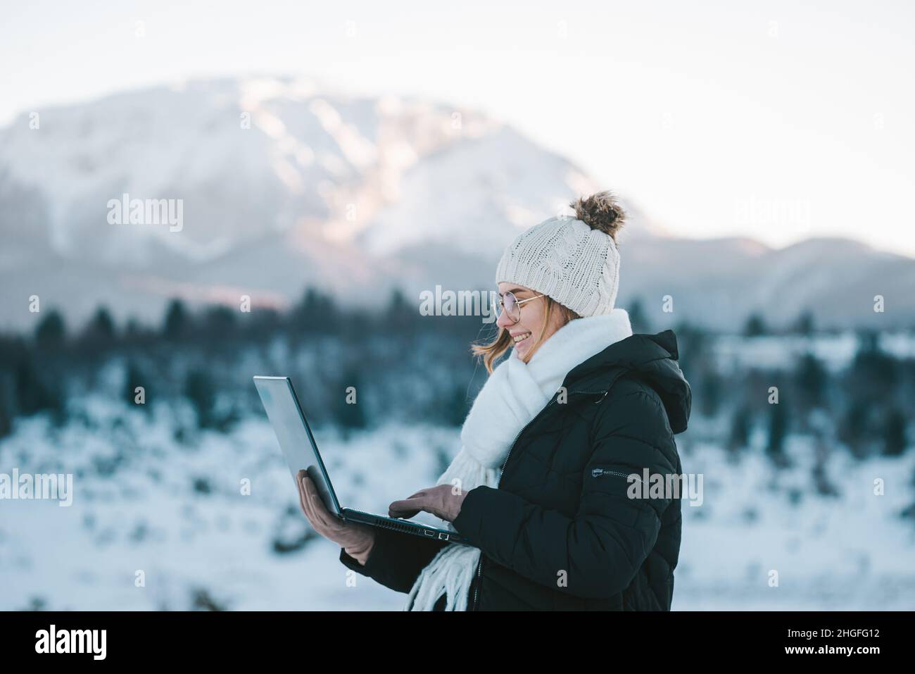 young smiling woman freelancer using laptop outdoors in snow mountains Stock Photo