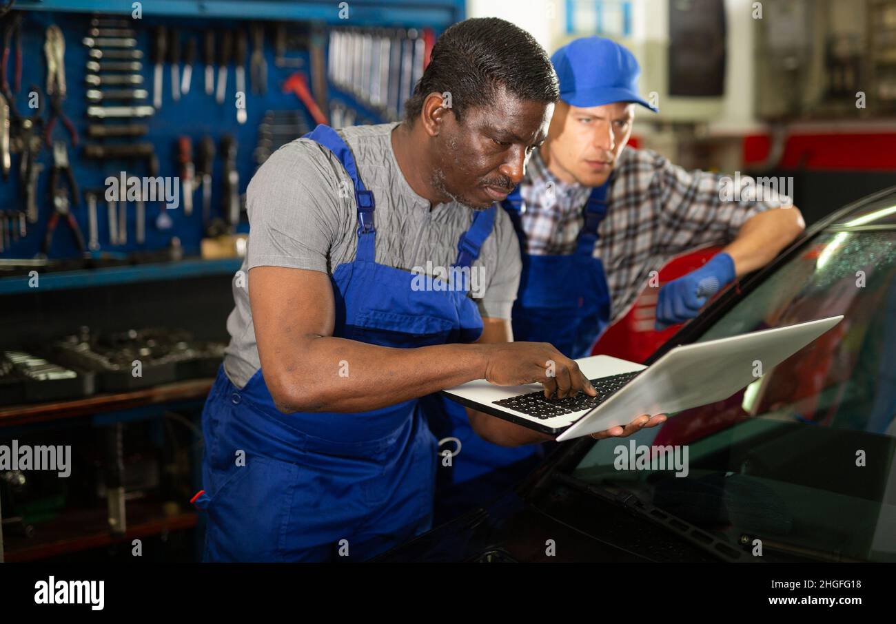 Two auto mechanics diagnosing car engine with laptop Stock Photo