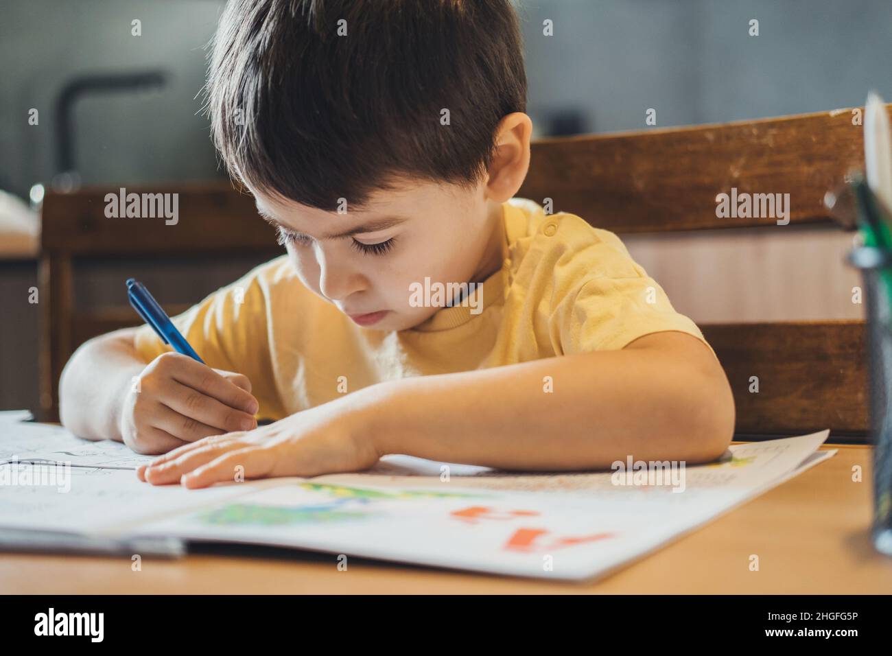 Little caucasian boy sitting at table and doing his homework for