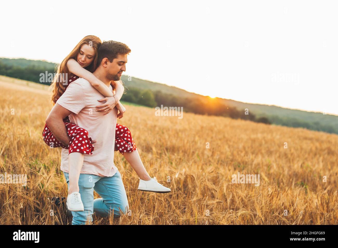 Caucasian man giving piggy back ride to his readheaded girlfriend in the wheat field. Stock Photo