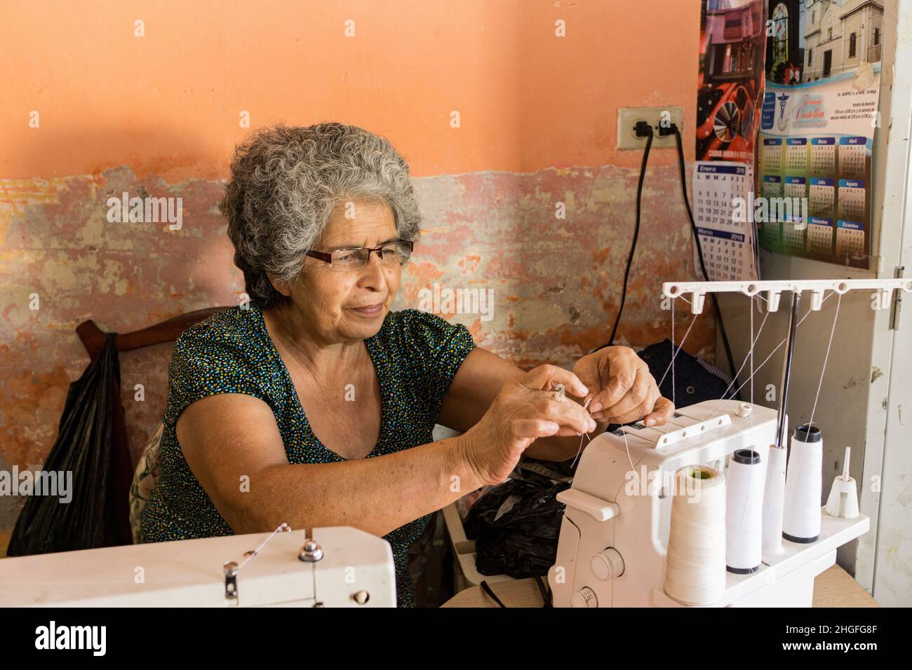 Nicaraguan seamstress threads  a serger in her workshop at the front of her home. Stock Photo