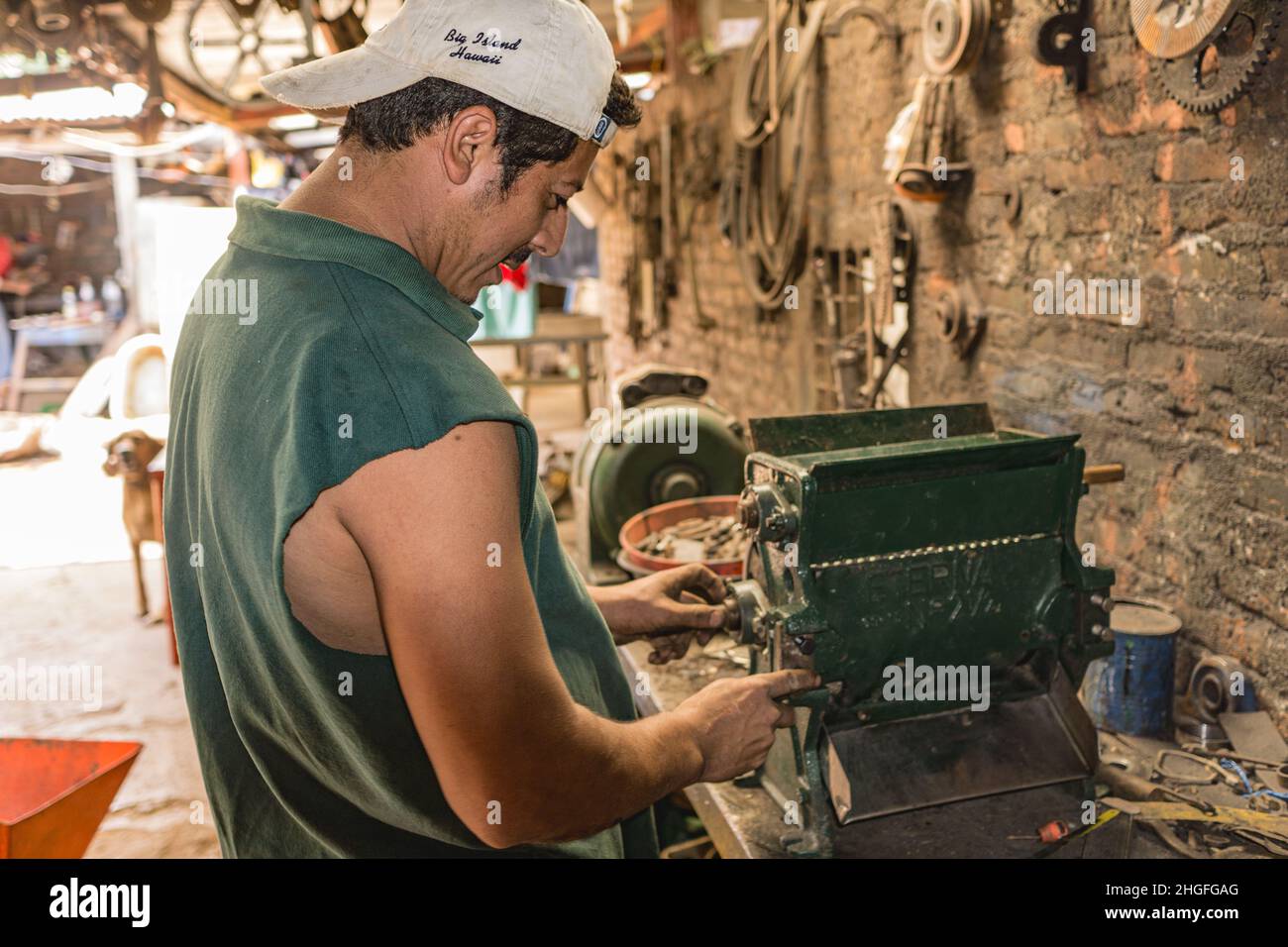 Man repairs a small coffee processing machine in a cluttered machine shop in Jinotega, Nicaragua. Stock Photo