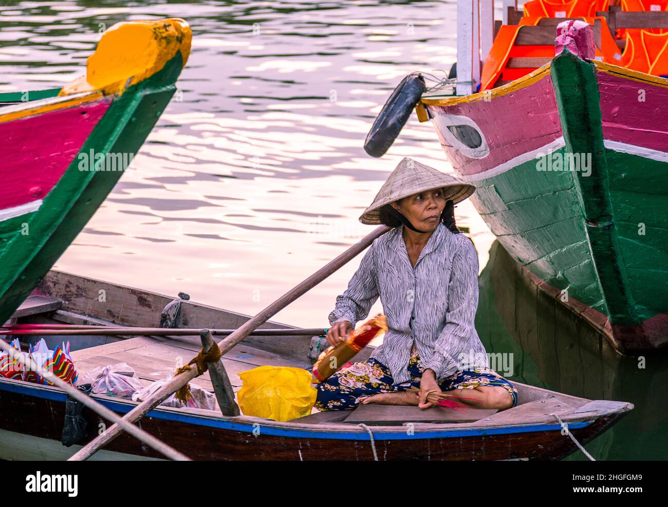 A small row boat and tour operator sits in her small boat between two larger green boats. Stock Photo