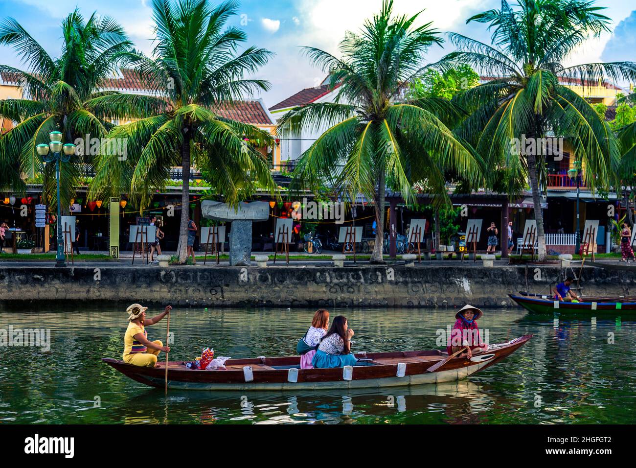 A small wooden tour boat goes down the Thu bon river carrying tourists by Old Town, Hoi An. Stock Photo