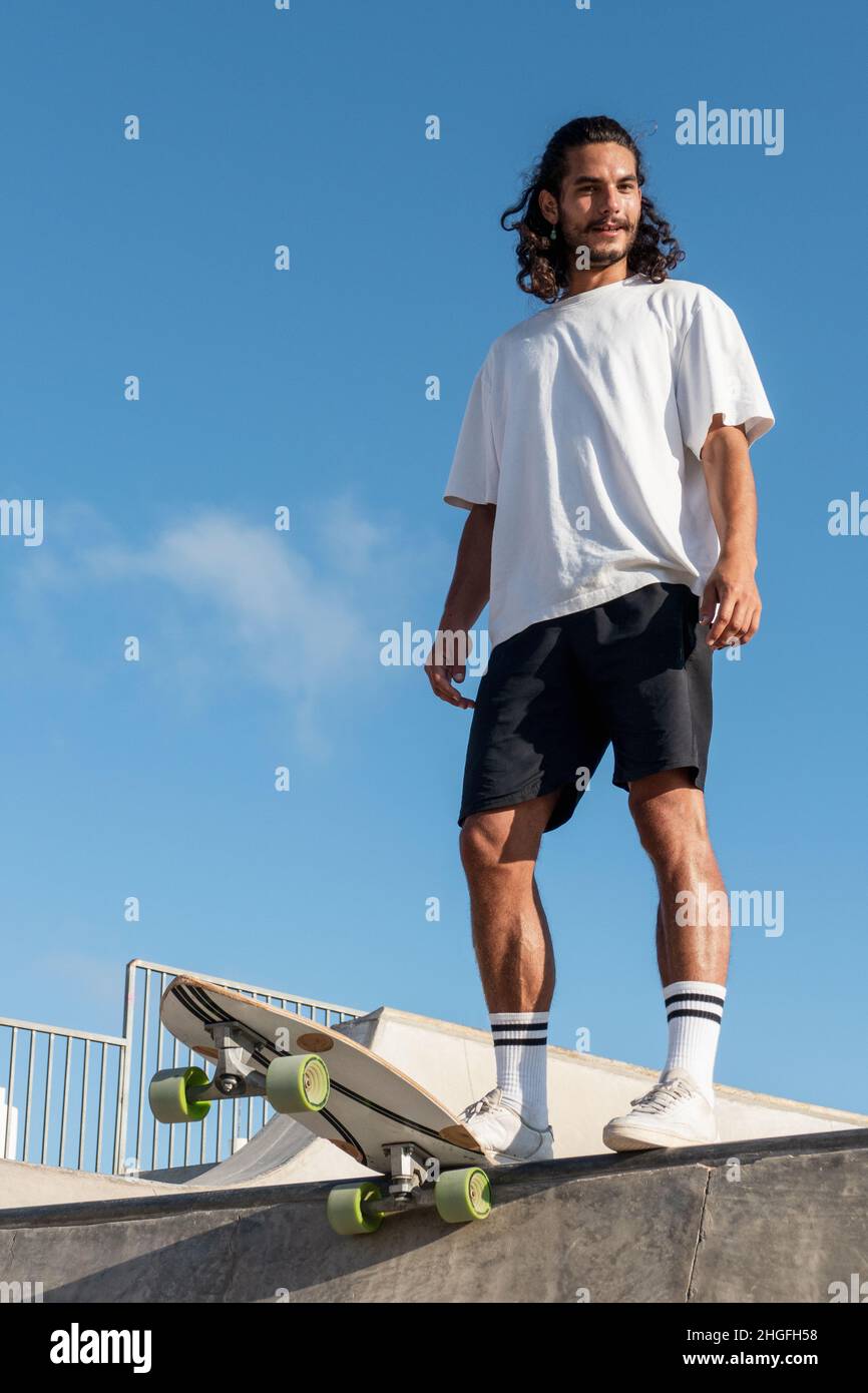 Young caucasian skater standing at the edge of the skate ramp. He is ...