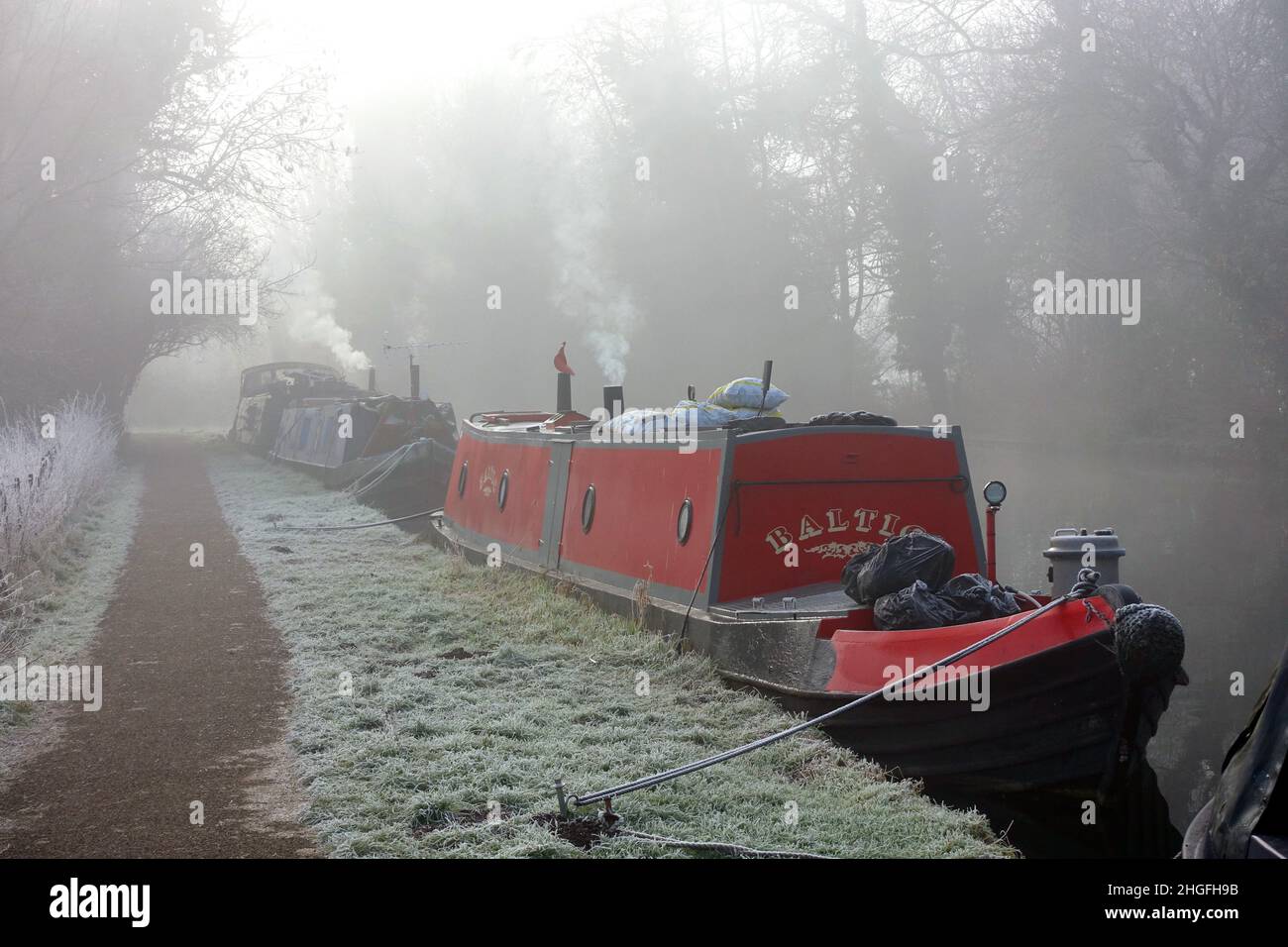 Smoke rising from chimneys on barges moored on the River Gade near Watford on a very cold foggy early winter morning in January Stock Photo