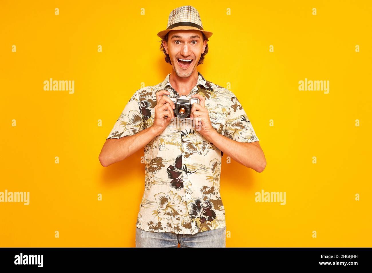 an excited male tourist traveler with his mouth open holds a camera in his hands in front of him. Stock Photo
