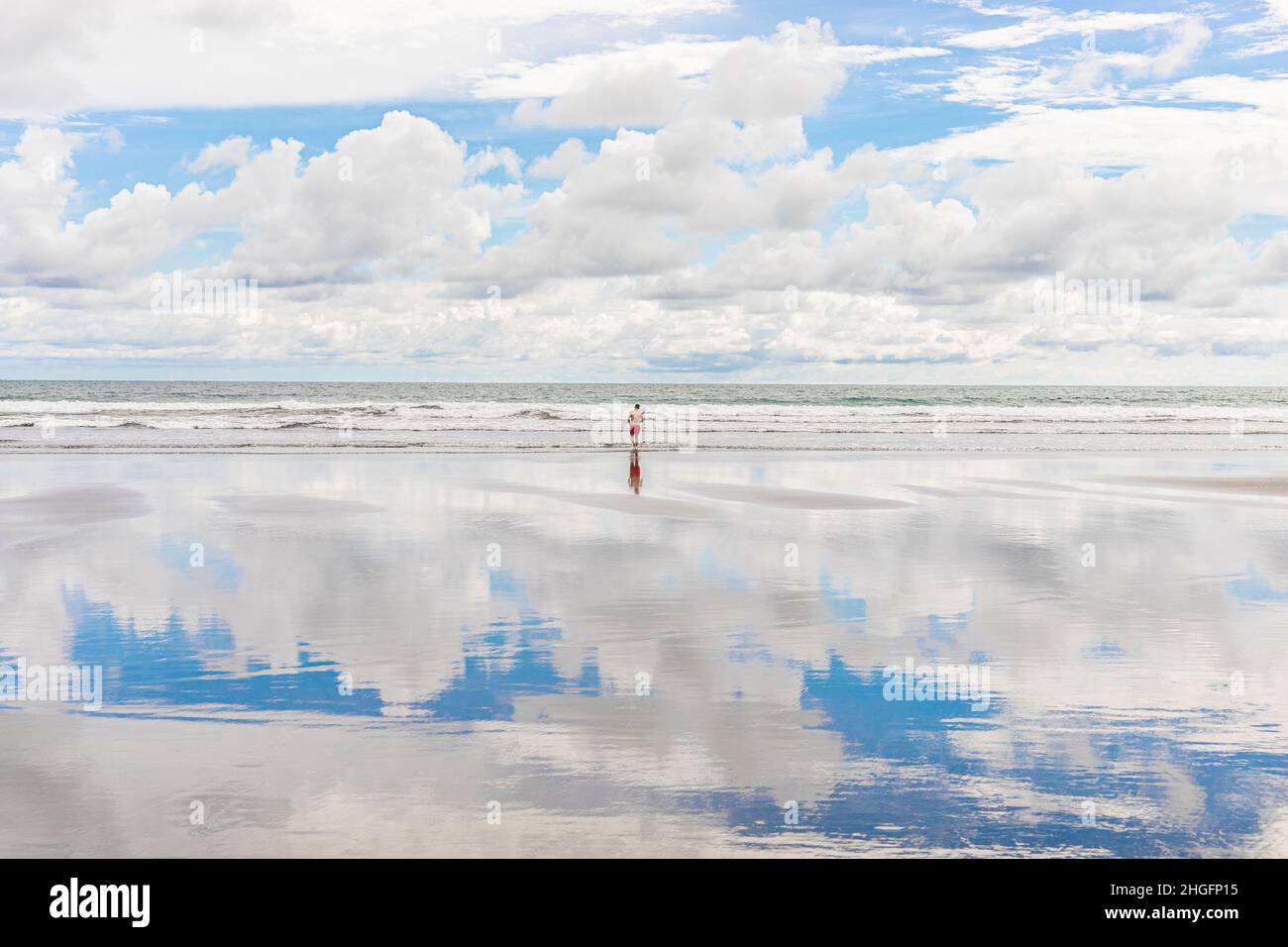 A man on a beautiful beach in Puntarenas, Costa Rica, the fluffy blue sky reflecting on the sand Stock Photo