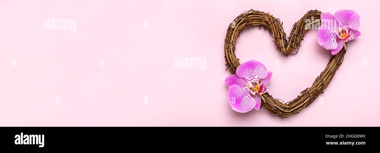 heart shaped rattan wreath decorated with tropical flowers of orchid on pink background Top view Flat lay Holiday card Happy Valentine's day, love con Stock Photo