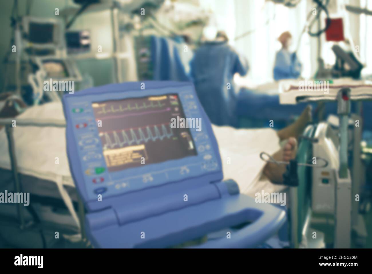 ECG monitor of patient in come on the background of doctors making emergency surgery to another patient in the ICU. Stock Photo