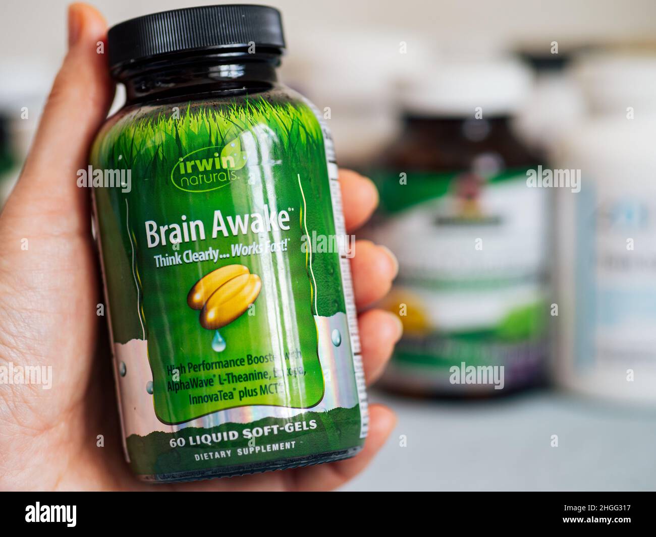 Moscow, Russia - March 09, 2021: Glass jar with Brain Awake capsules in female hand and others nutrition supplements in blurred background. Brain Awake by Irwin Naturals is complex for boost brain function Stock Photo