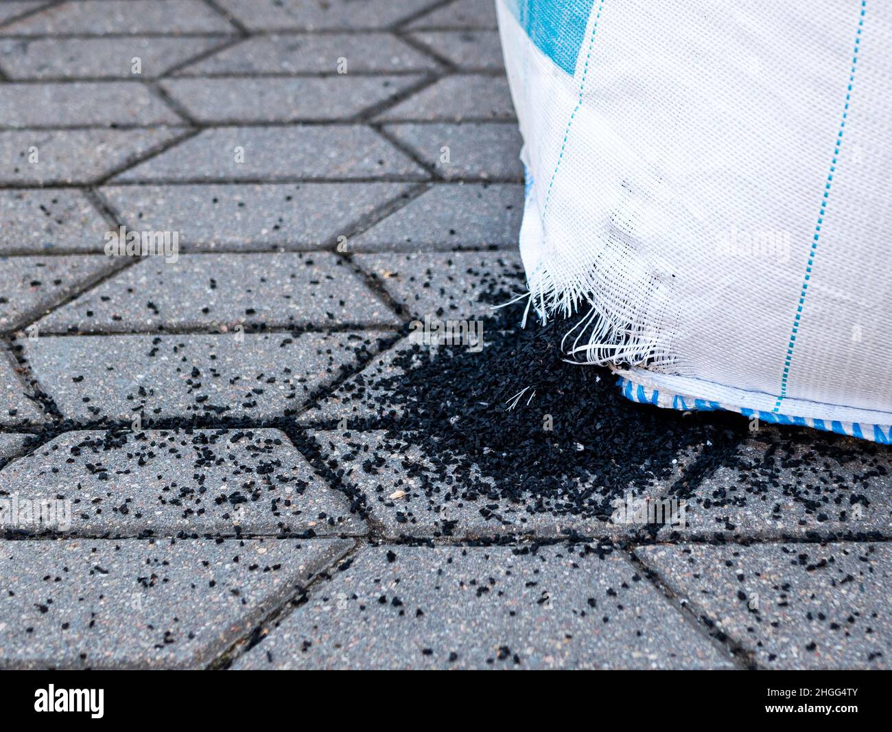 Black polystyrene granules escape from damaged packaging. Crumbs of the are on the ground. Concept of mismanaged property, diseconomy Stock Photo