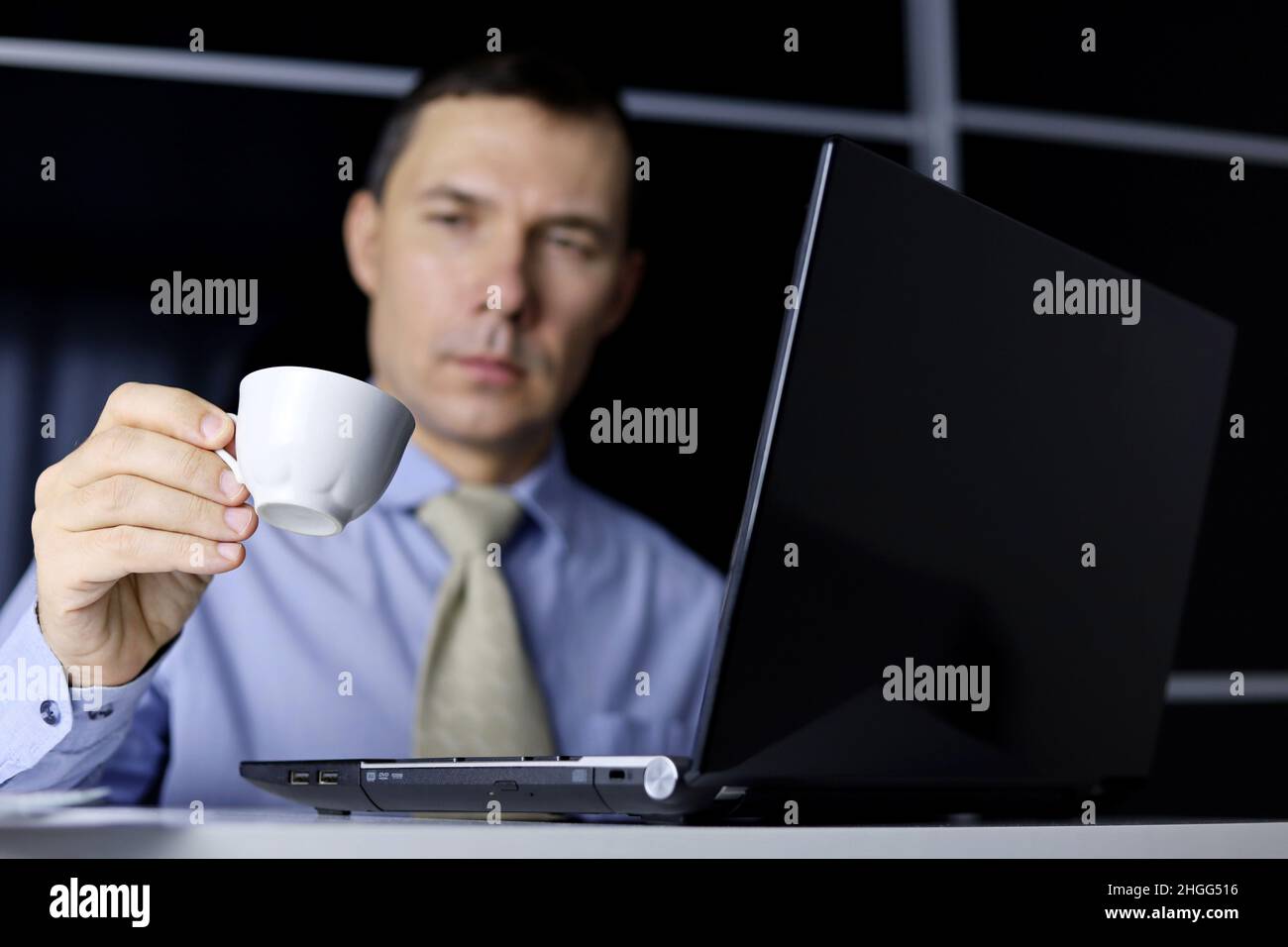 Coffee cup in hand of man sitting at laptop. Enjoying the hot drink, break during work in office Stock Photo