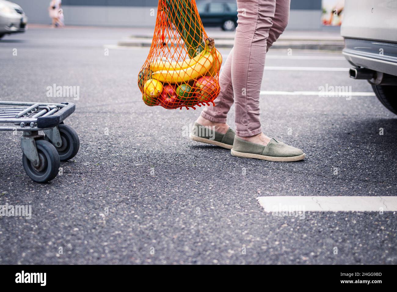Reusable mesh bag with groceries purchased. Woman standing at parking lot after plastic free shopping at supermarket. Ethical consumerism and sustaina Stock Photo