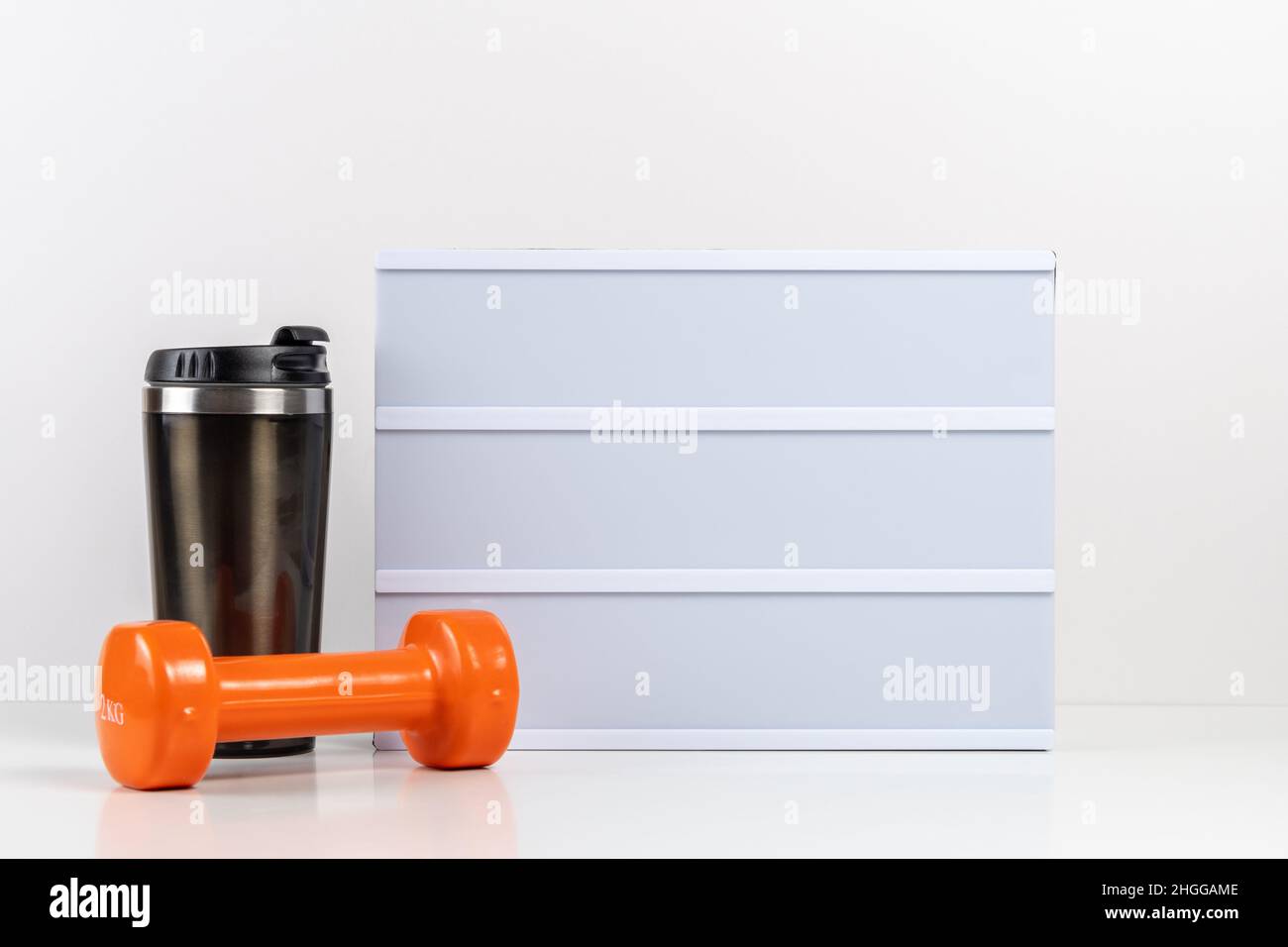 Fitness dumbbells with empty lightbox on white table. Mockup concept. Stock Photo