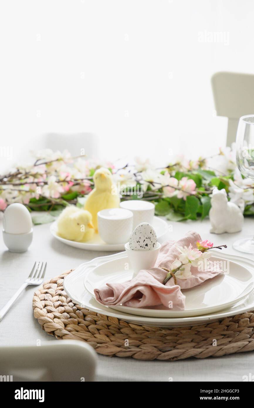 Easter table setting with yellow chick, spring natural decorations, fresh flowers and eggs. Elegance dinner at home interior. Close up. Christian reli Stock Photo