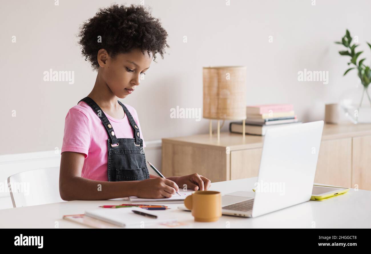 Cute little girl studying online. Kid drawing and using laptop at home. Modern learning, children lifestyle, study online concept Stock Photo
