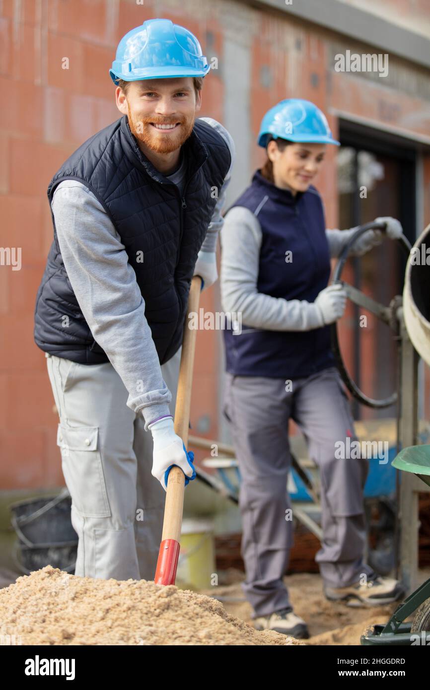 male and female workers on outdoor site using cement mixer Stock Photo