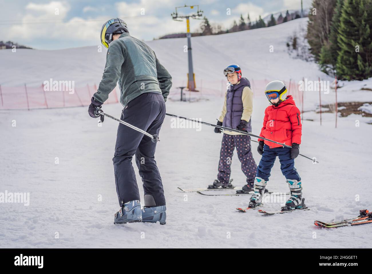 Mom and son are learning to ski with an instructor. Active toddler kid with safety helmet, goggles and poles. Ski race for young children. Winter Stock Photo