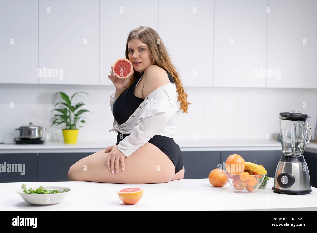 Tasty vitamins concept. Weight loss, detox, body cleansing, slagging, weak immunity. Possibility to build. Attractive girl in kitchen with grapefruit in her hands is preparing to prepare a smoothie. High quality photo Stock Photo
