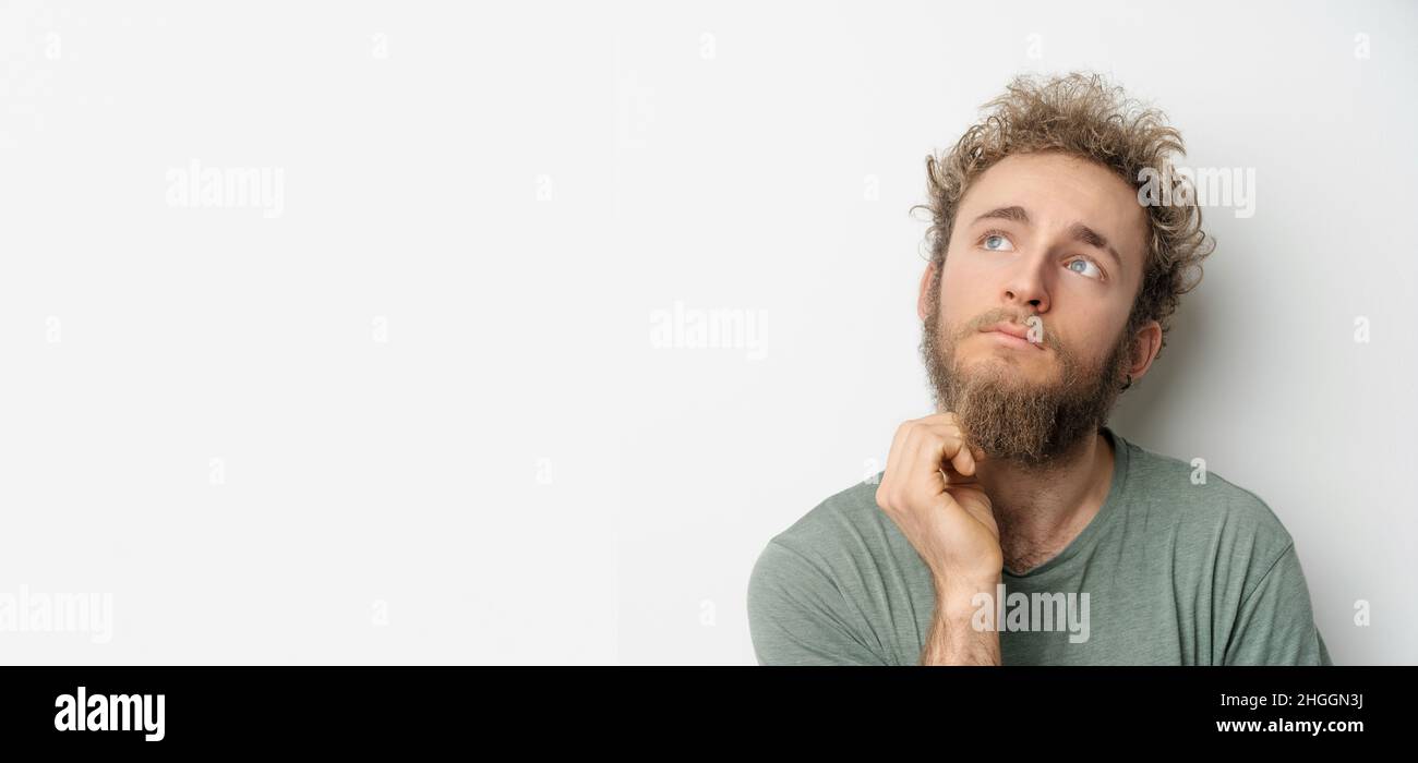 Young guy looks up thoughtfully against a background. Concept of thinking, deciding, weighing, pros and cons. Copy space. High quality photo Stock Photo
