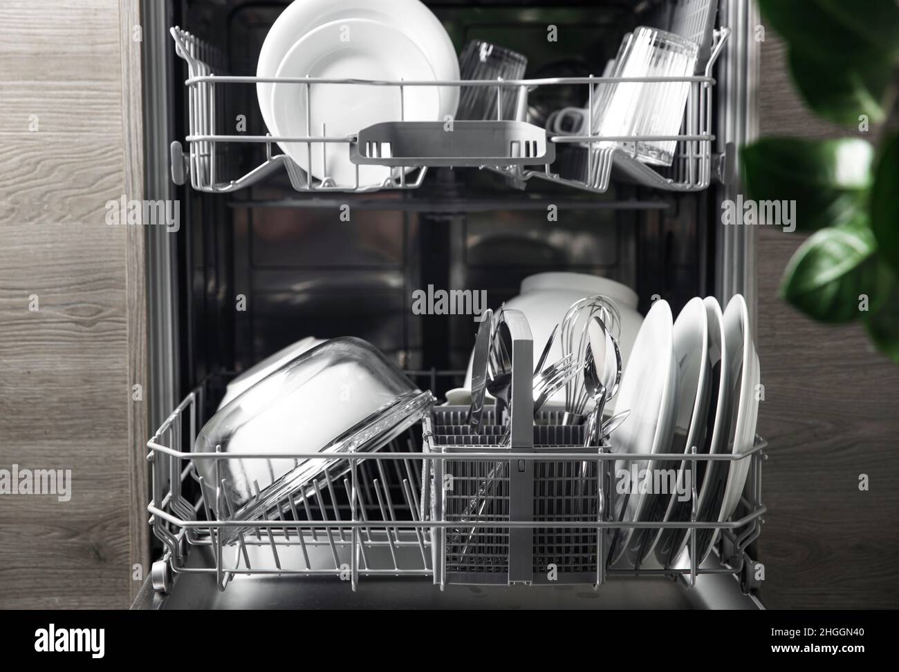 Front view of open automatic stainless steel built-in fully integrated top control dishwasher range machine with clean utensils, cutlery, glasses, dishes, plates inside in modern home kitchen Stock Photo