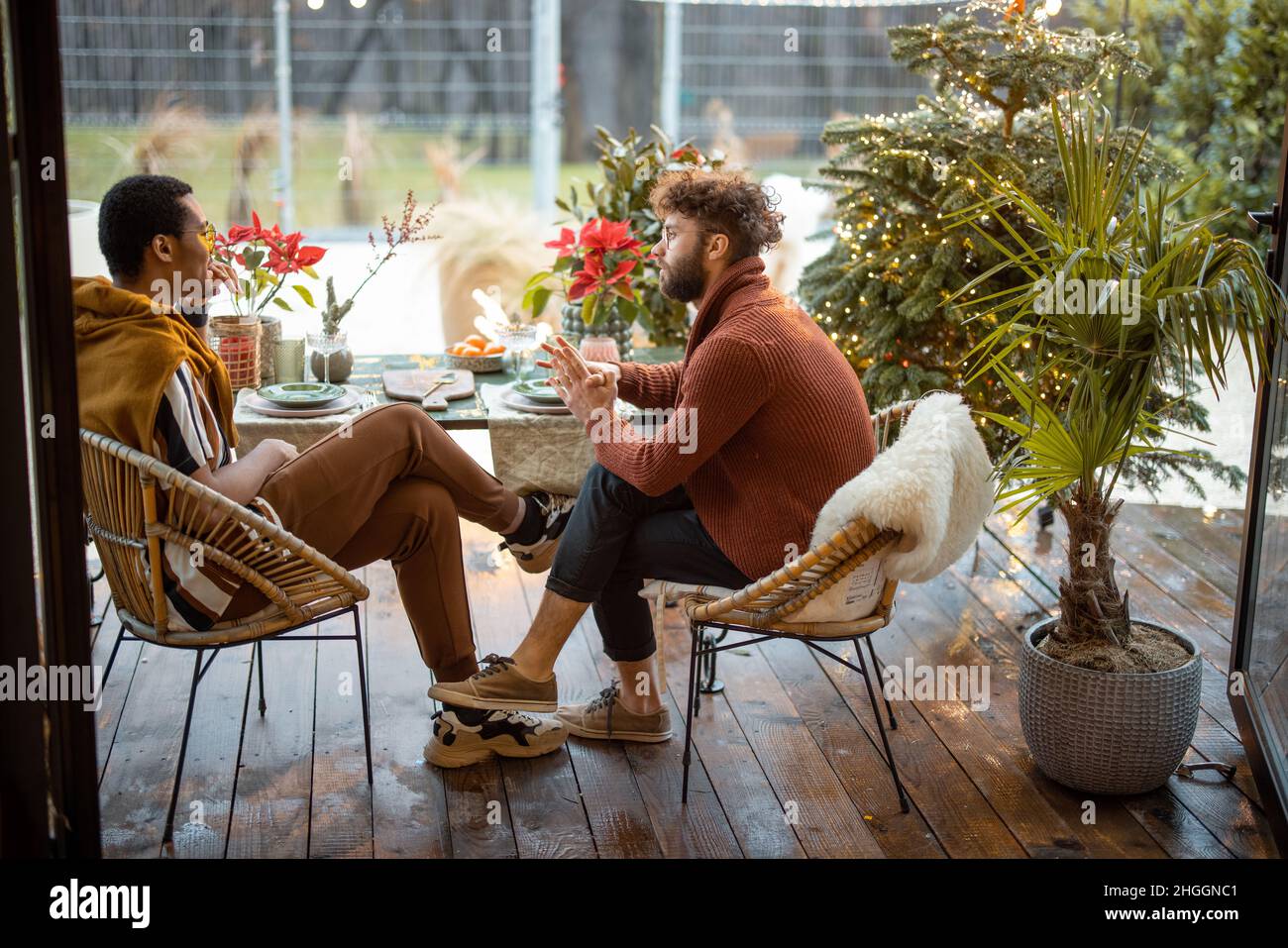 Two multiracial male friends having close conversation, sitting by a dinner table at backyard Stock Photo