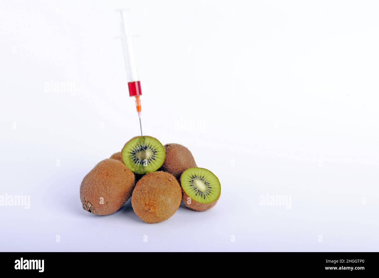 kiwi fruit, Chinese gooseberry (Actinidia deliciosa), fresh kiwis, partly halved, syringe stuck in kiwi, genetically modified fruit Stock Photo