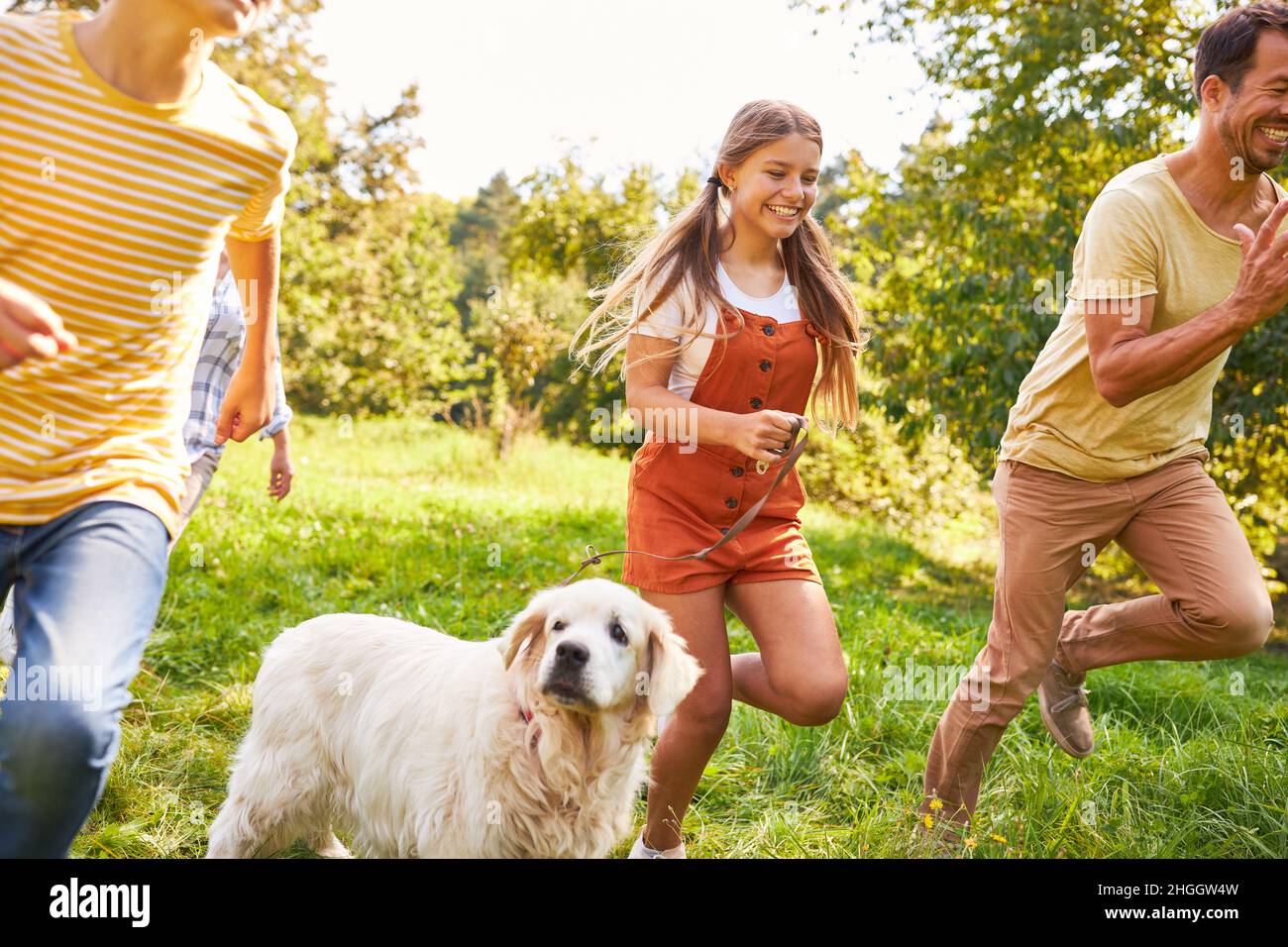Girl and dog running with family in park in summer in nature Stock Photo