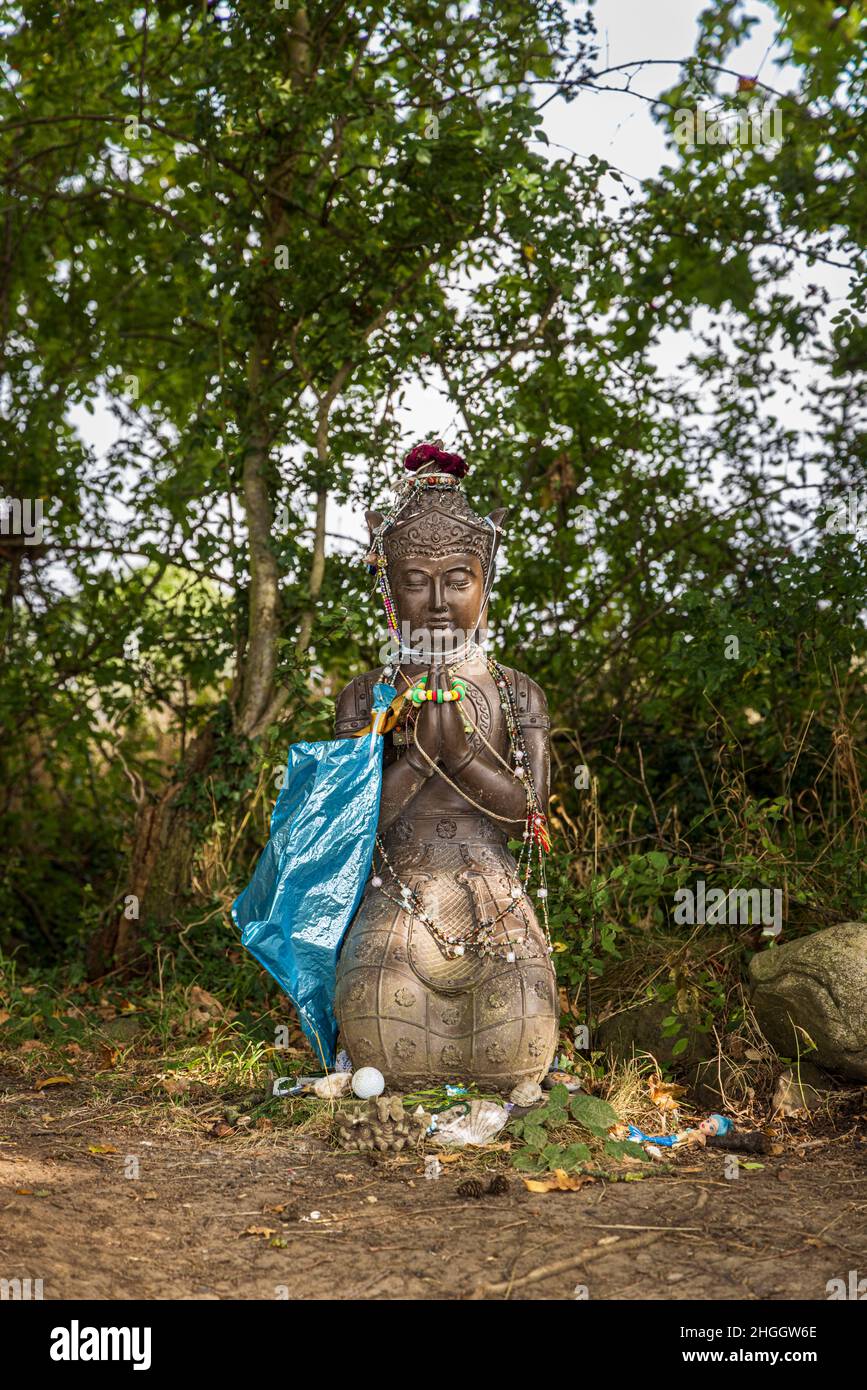 Buddha figure with hands clasped in prayer pose on knees and decorated with various items left by visitors in a field near Thirsk, Yorkshire, England Stock Photo