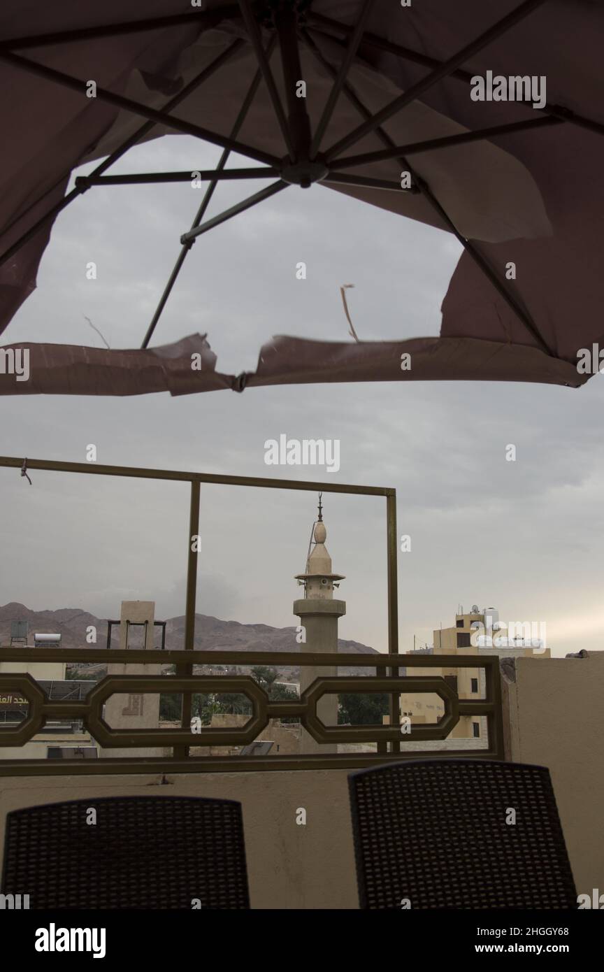 View of a mosque in Aqaba Jordan with grayish blue skies at the Red Sea through a torn umbrella awning at sunrise. Stock Photo