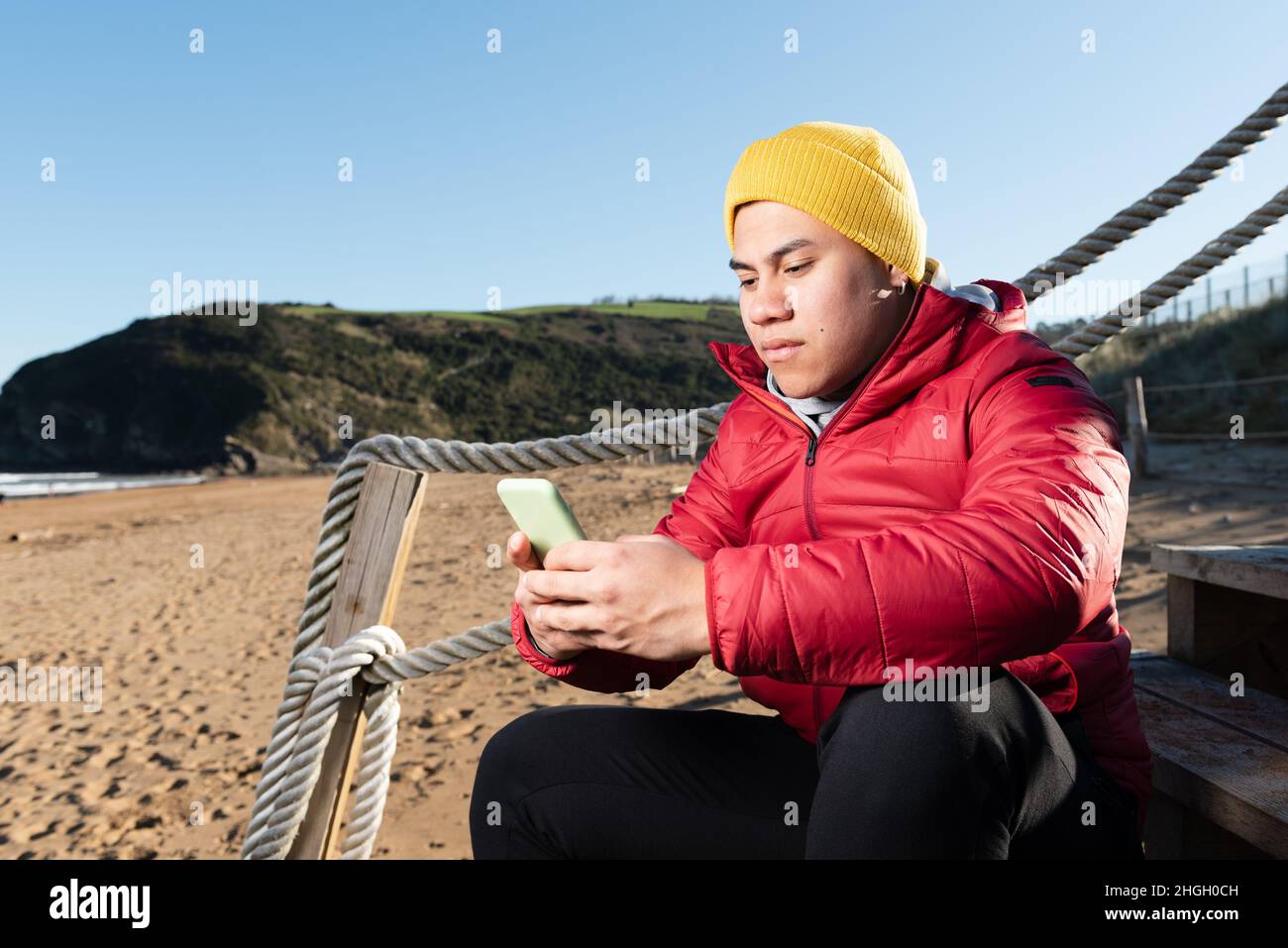 Latin man chatting on phone sitting on stairs at beach Stock Photo
