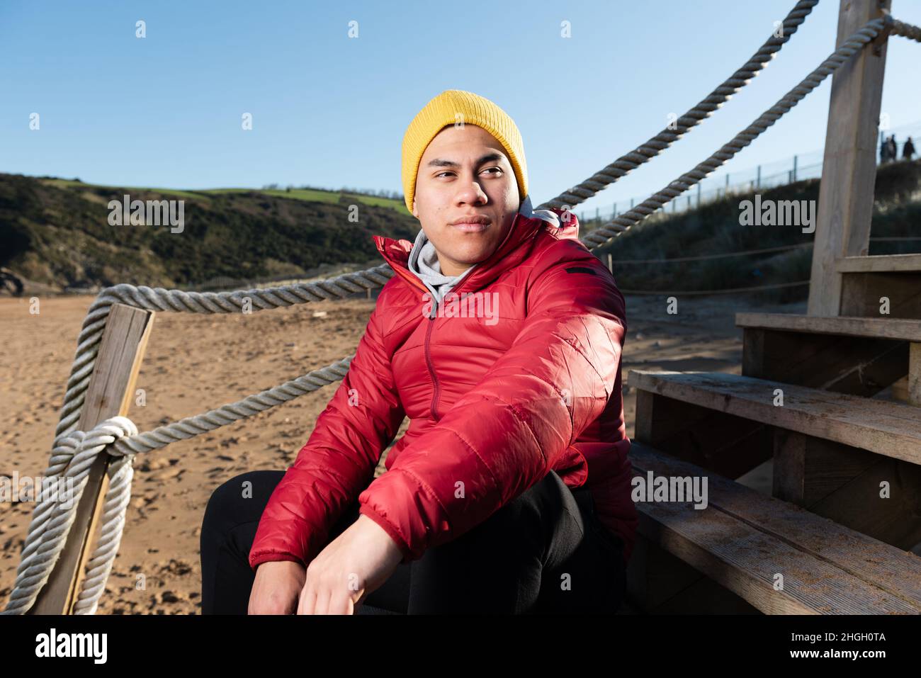 Portrait of young latin man wearing winter clothes and sitting on stairs Stock Photo