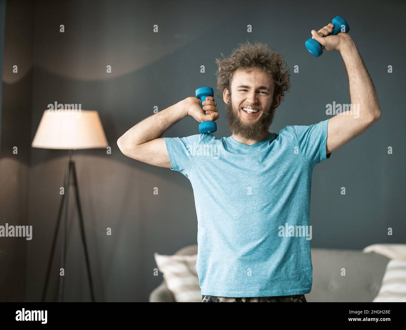 Handsome Man Does Fitness with Dumbbells At Home. Guy Keeps Fit During Quarantine. Gray background. High quality photo Stock Photo